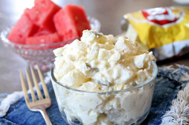 potato salad in bowl with watermelon and chips in background