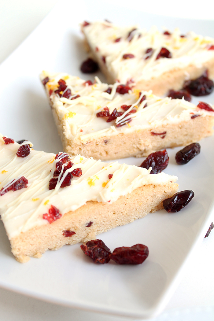 Three Cranberry Bliss Bars cut into triangles on a white plate with extra craisins on the plate. 