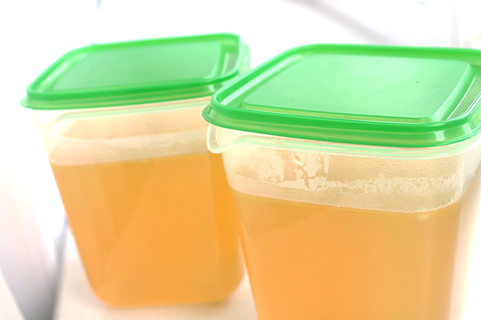 Two containers of chicken stock. They are plastic with green lids