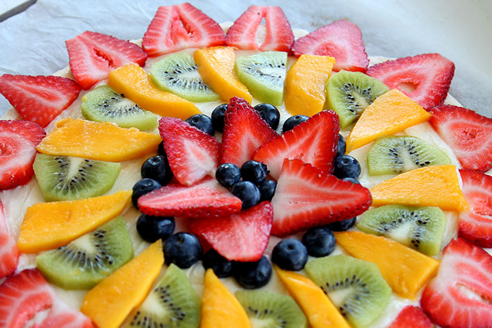 upclose shot of fruit pizza decorated with strawberries, blueberries, kiwis and mango