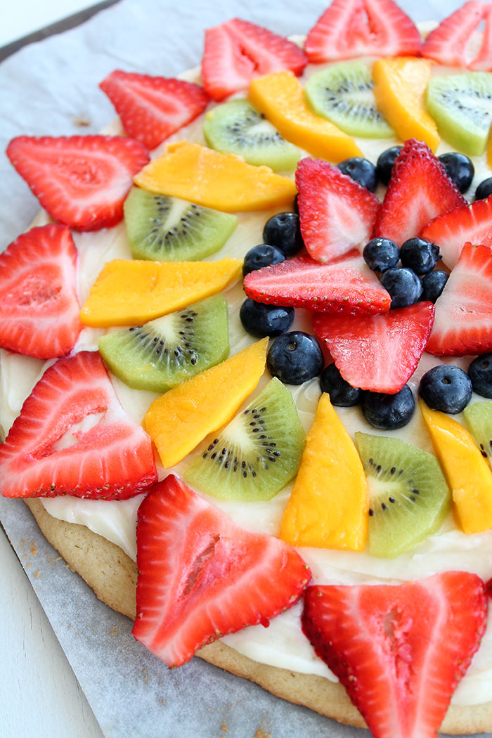 Fruit Pizza, Large sugar cookie with white frosting and fruit on top. You can only see half of it in the picture and the fruit is arranged in a pretty pattern. Very colorful.