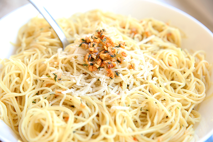 White bowl of angel hair pasta tossed with golden garlic and freshly grated Parmesan cheese. 