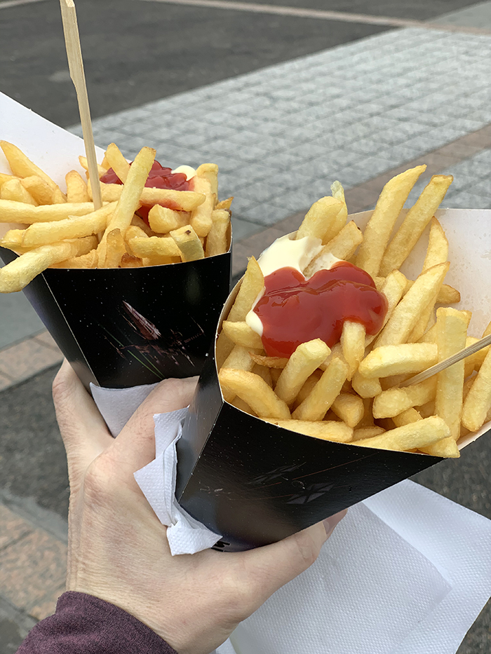 Golden French Fries in carry cups with ketchup and mayonaise squirted on top. And a little wooden fork to eat them with