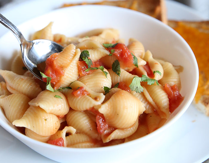 Instant Pot Macaroni and tomatoes in a white bowl with a spoon taking a bite. 