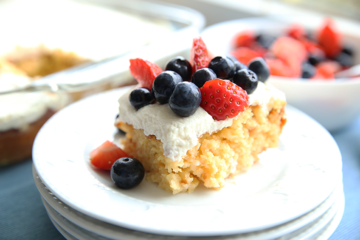 Tres Leches Cake on a white plate with whipped cream and berries