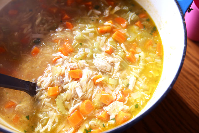 stock pot of soup that contains chicken, orzo pasta, celery, onions and chicken and lemon
