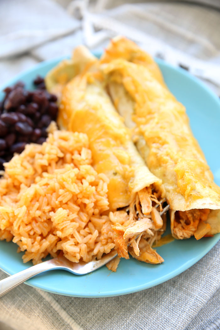 Blue plate with two enchiladas rice and beans and a fork taking a bite