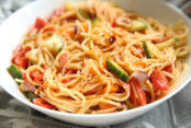 A bowl of spaghetti noodles mixed with veggies and italian salad dressing with salad supreme spice tossed together to make a pasta salad. It is in a white bowl.