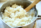 Picture of a metal 2 quart sauce pan with cooked coconut rice in it and a wooden spoon about to take a big scoop out.