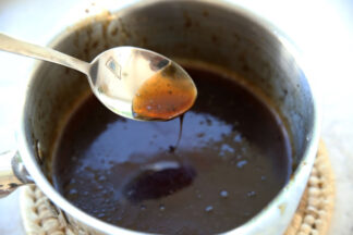 small silver sauce pan with cooked teriyaki sauce in it. There is a spoon dipped in to show the consistency of the sauce