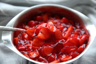 Strawberries mixed in with danish dessert in a 1 quart stainless steel sauce pan. there is a spoon taking a scoop out.