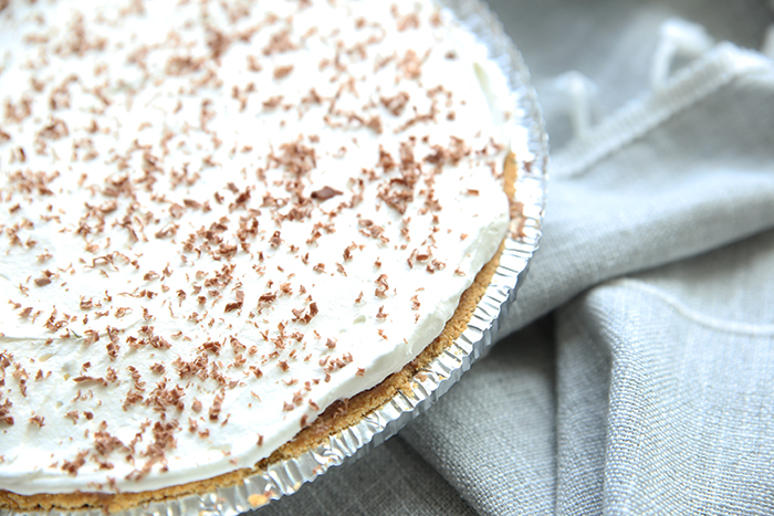 a french silk pie that has not been cut into. It is covered with cool whip and sprinkled with grated chocoalte