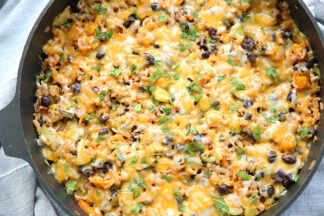 large skillet full of a cheese covered skillet dinner with zucchini and black beans and rice