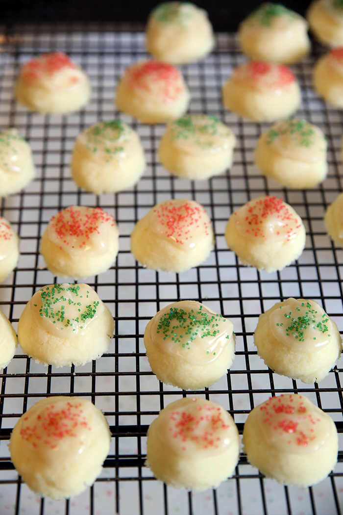 a cooling rack that has lots of small meltaway cookies on it. the cookies are frosted and have green and red sprinkles on them.