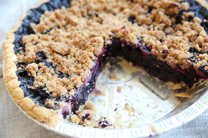 Blueberry pie with crumble topping and two slices taken out. you can see the beautiful purple/blue center of the pie