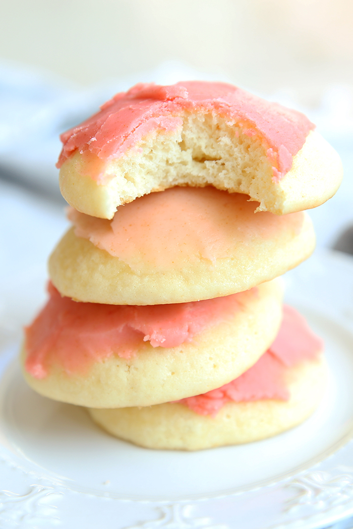 Four cookies with pink frosting on a small white plate. the top cookie has a bite out of it. 