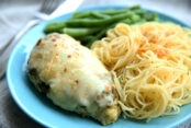a juicy chicken breast with seasoning and cheese next to noodles and green beans