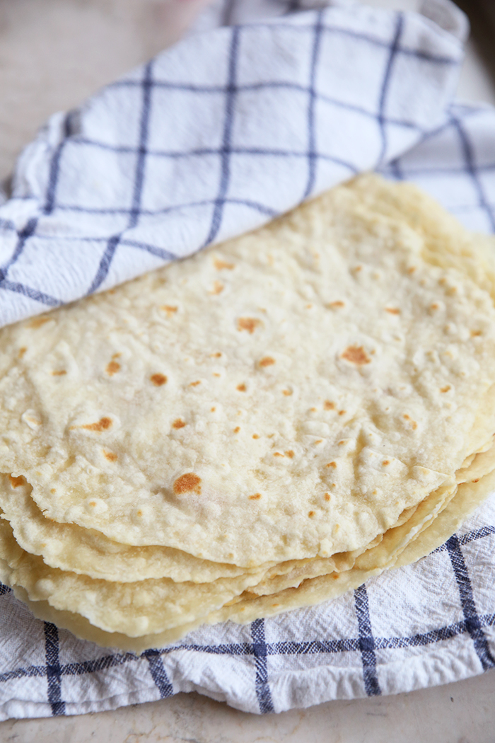 Homemade flour tortillas wrapped in a hand towel that is blue and white plaid.