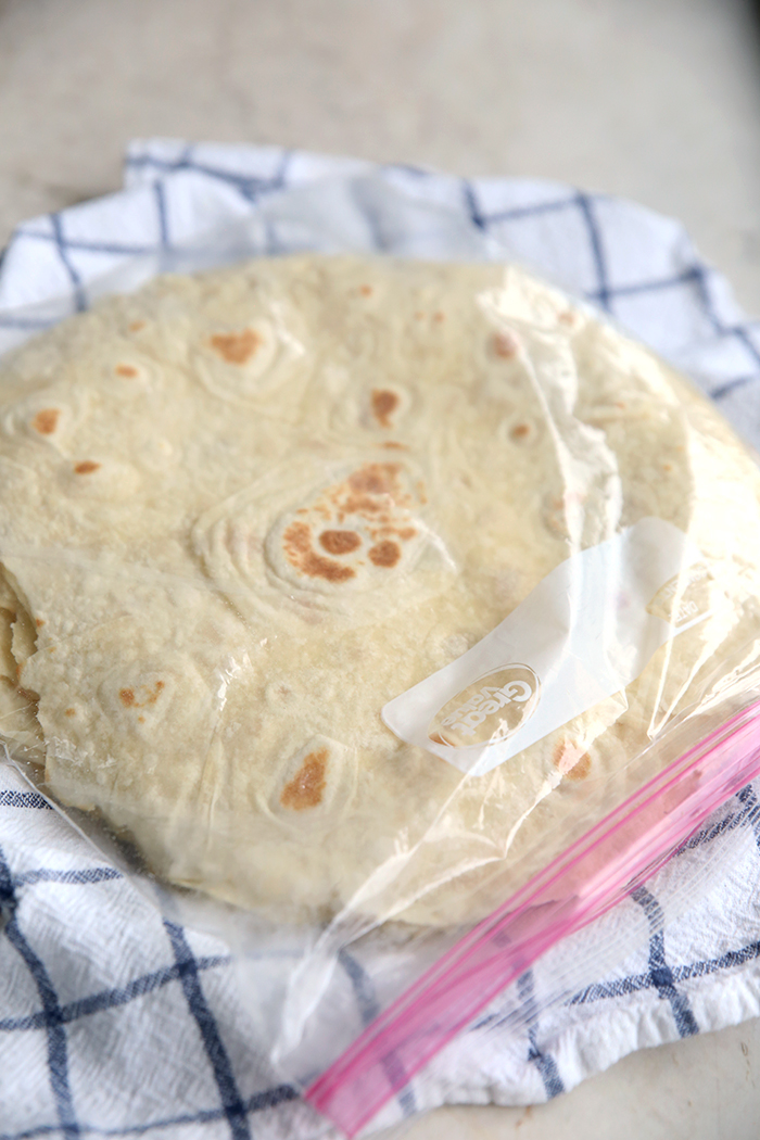 Homemade flour tortillas placed inside a ziploc bag, sitting on top of a white and blue towel.