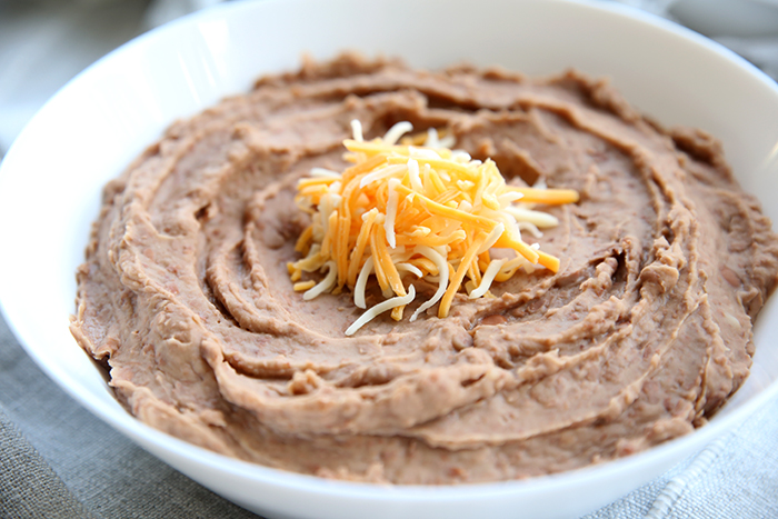 Picture of homemade refried beans, in a white bowl topped with shredded cheese