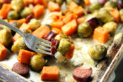 Sheet pan of brussel sprouts, sweet potatoes and Kielbasa with a fork taking some of the food off the sheet pan