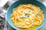 Egg and spaghetti soup in a blue with a grey napkin on the left side of the bowl. A spoon is sitting on top of the grey napkin on the left.