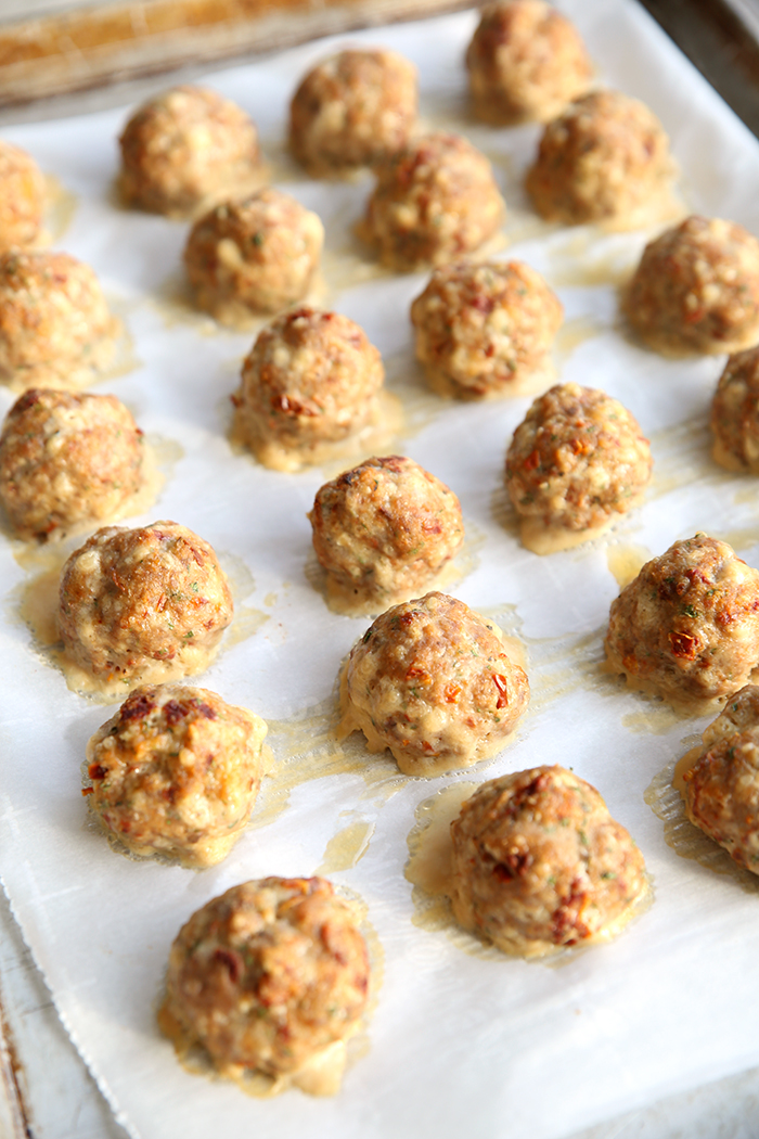 A partial picture of a cookie sheet lined with parchment paper with Sun-dried Tomato Turkey Meatballs in several rows.