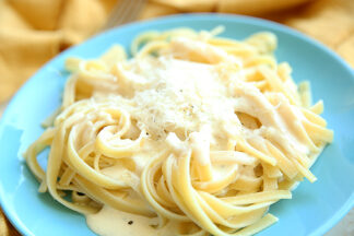 Fettuccini sitting on a blue plate topped with Alfredo sauce and grated Parmesan cheese.