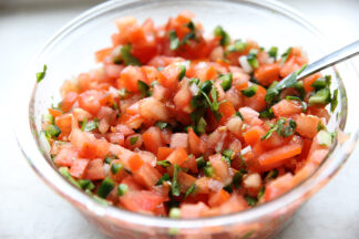 A glass bowl filled to the top with Pico de Gallo with the handle of a spoon sticking out of it.