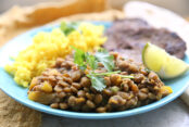 a blue plate holding a serving of ecuadorian lentil stew, carne asada, and ecuadorian yellow rice and a slice of lime