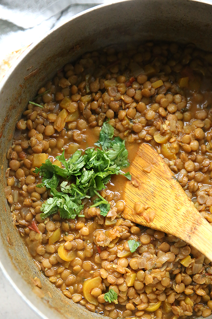 a silver pan with ecuadorian lentil stew in it and a wooden spoon with cilantro chopped and on the surface