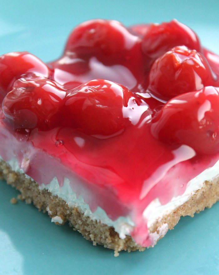 A photo of No-Bake-Cherry-Cheesecake. It has a graham cracker crust and a cream cheese layer topped with cherry pie filling. It is on a blue plate.