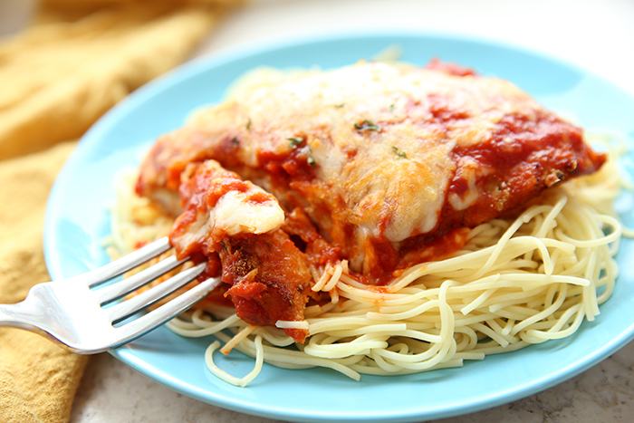 A blue plate of spaghetti and baked parmesan chicken with a fork holding a bite of the food. 