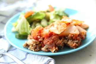 A blue plate with a serving of cabbage roll casserole and a dinner salad on a table with a blue and white tablecloth