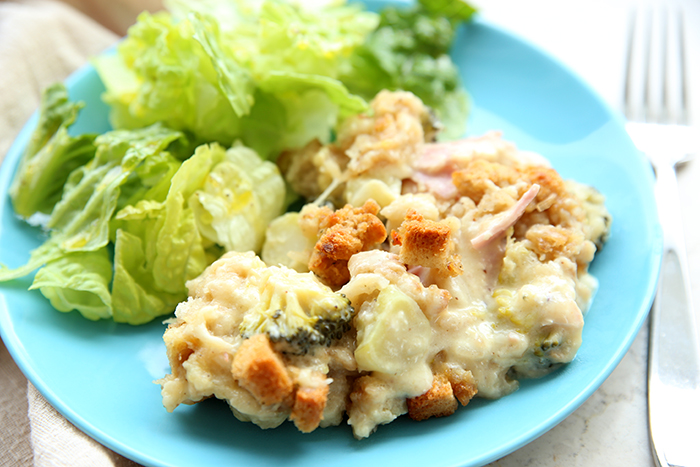 A blue plate with a serving of chicken casserole and romaine lettuce with a fork on the right side of the plate. There's a beige napkin in the background on the left side of the plate.