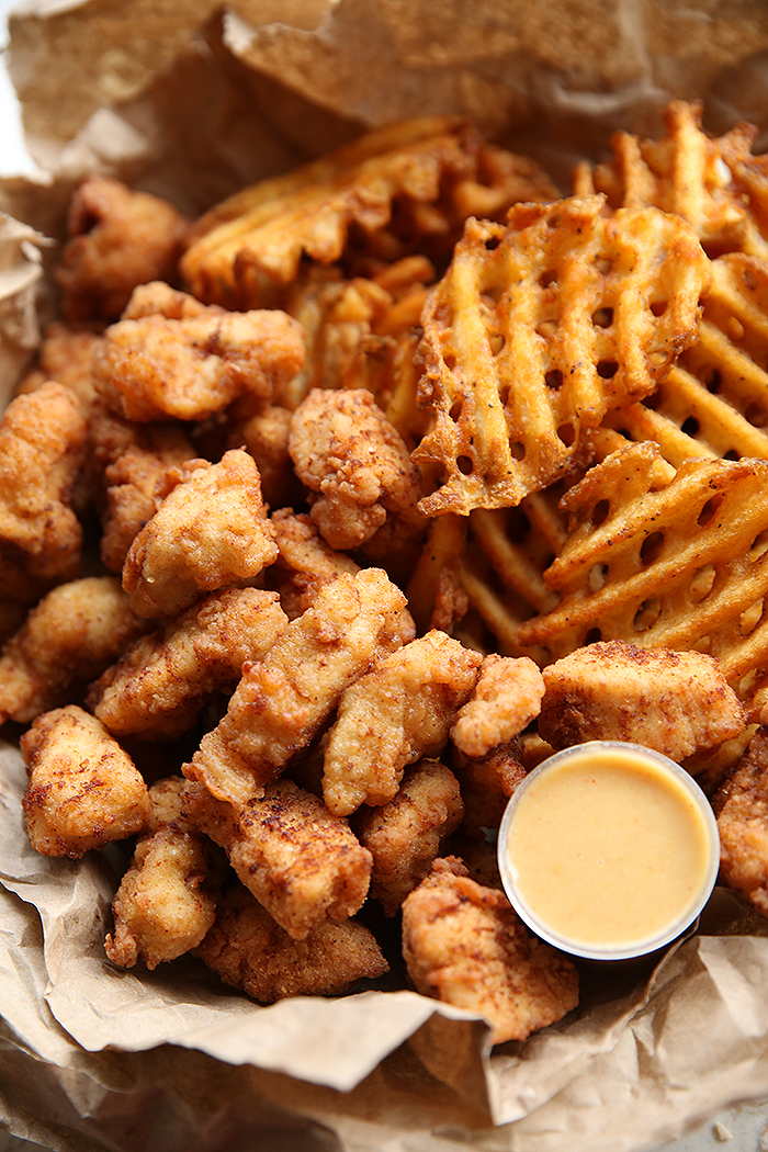 A closeup photo of Chick-fil-A Nuggets with waffle fries and a small cup of dipping sauce in a bowl lined with brown paper.