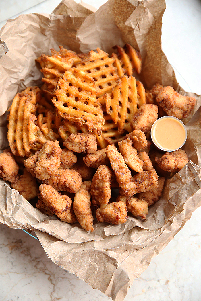 A basket lined with brown paper filled with Copycat Chick-fil-A Chicken Nuggets and waffle fries with Chick-fil-A dipping sauce in a little cup.