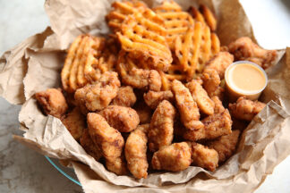 Chick-fil-A Chicken Nuggets with waffle fries in a basket lined with brown paper. There's a small plastic cup of dipping sauce in the basket.
