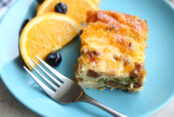A blue plate with a serving of easy cheesy breakfast casserole, oranges and blueberries and a silver fork on the left side