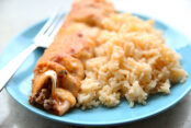 A blue plate topped with one enchilada, a fork and Spanish Rice.
