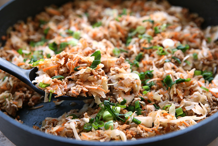 A partial picture of a pan of Egg Roll in a Bowl recipe with a black spoon taking a scoop out.