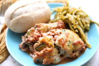 A serving of lasagna, green beans and a roll on a blue plate with a yellow napkin on the left side and top in the background.