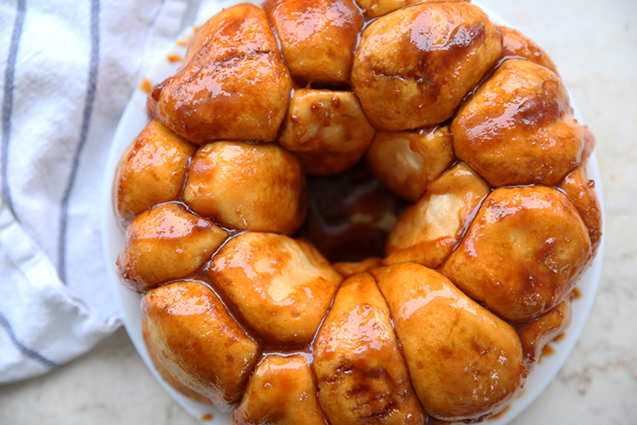 Butterscotch Monkey Bread sitting on a white plate with a white and blue striped kitchen towel in the background on the right.