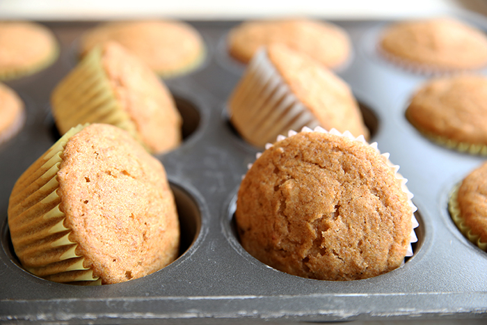 A horizontal photo of a partial picture of a muffin pan filled with bran muffins with four muffins tilted on the side.