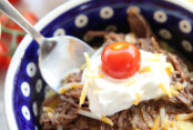 A serving of Instant Pot Beef Sundaes in a blue bowl with a spoon digging in to take a bite.