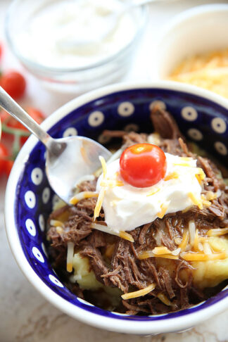 A serving of Instant Pot Beef Sundaes in a blue bowl with a spoon digging in to take a bite.