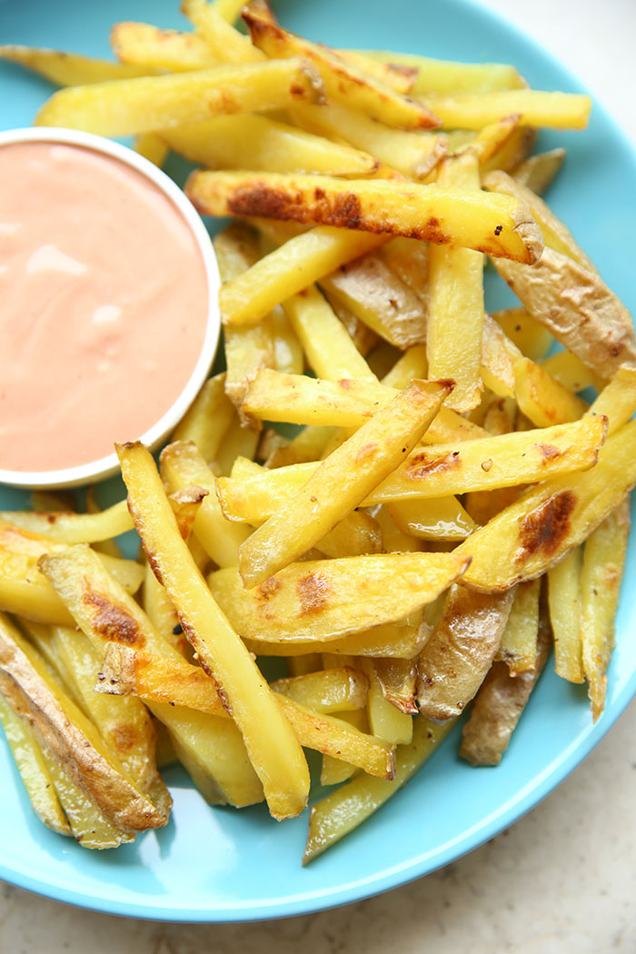 A blue plate full of baked French Fries with a small cup filled with French Fry sauce.