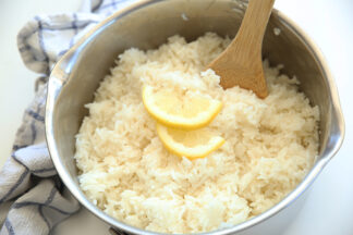 Lemon rice in a large pot with a large wooden spoon sticking out and up from the rice and a couple of halved slices of lemon on top of the rice.