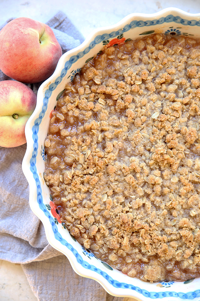fresh peach crisp right out of the oven ready to serve out of a pretty pie dish
