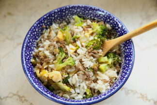 A dark blue polish pottery bowl with a white dot pattern filled with broccoli beef fried rice. A wooden serving spoon is placed diagonally in the bowl on the right side.